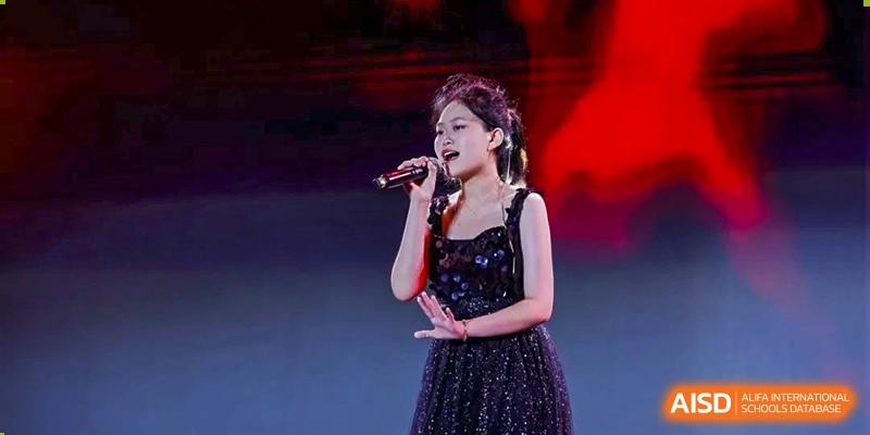 A solo female singer performing a song on stage, dressed in a sparkling black outfit, at an event for The Experimental School Affiliated with Zhuhai No.1 High School.