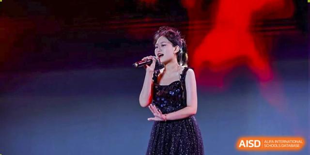 A solo female singer performing a song on stage, dressed in a sparkling black outfit, at an event for The Experimental School Affiliated with Zhuhai No.1 High School.