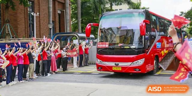 A large red bus parked with students and staff standing nearby, likely for a field trip or event organized by The Experimental School Affiliated with Zhuhai No.1 High School.