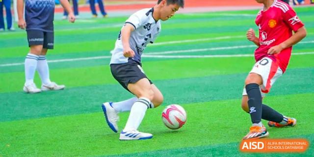 A student from The Experimental School Affiliated with Zhuhai No.1 High School skillfully dribbling a soccer ball on the green turf field.