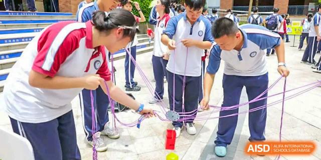 Students from The Experimental School Affiliated with Zhuhai No.1 High School engaging in a team-building exercise involving ropes and movement.