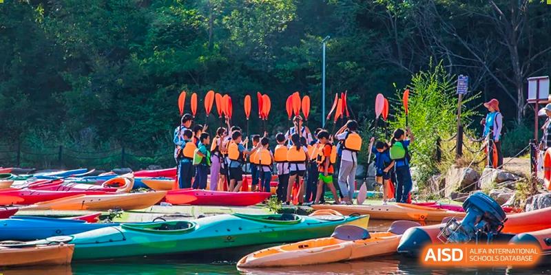 Beijing Keystone Academy students in life jackets with kayaks and paddles, gathered by the water for an outdoor activity.