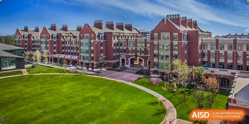 A beautiful, green campus at Beijing Keystone Academy, showing a large brick academic building and a well-maintained lawn.