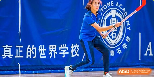A Beijing Keystone Academy student performing a dance on stage with a large banner in the background.