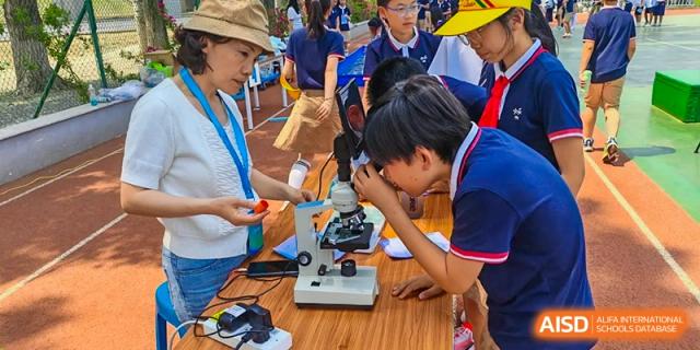 A group of Beijing Zhongguancun Foreign Language School students using a microscope during a science class.