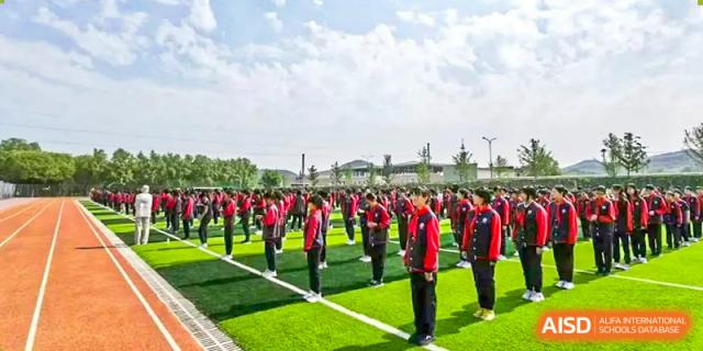 A photo showing a large group of students in red shirts doing a synchronized outdoor activity, at Beijing Zhongguancun Foreign Language School.