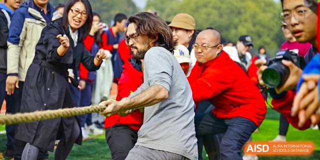 A team of students and faculty from Beijing Zhongguancun Foreign Language School competes in a tug-of--war match on a grassy field.