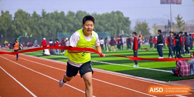 A student from Beijing Zhongguancun Foreign Language School sprints to the finish line, breaking a red ribbon during a track and field event.