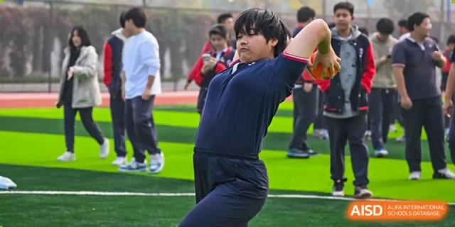 A student from Beijing Zhongguancun Foreign Language School winds up to throw a shot put on a sports field.