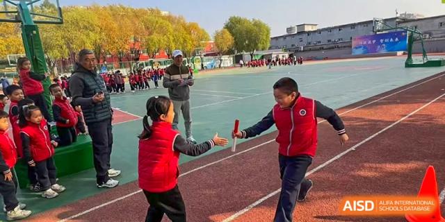 Two students from Beijing Zhongguancun Foreign Language School participate in a relay race, exchanging a baton on a running track.