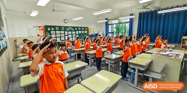 A dynamic view of a classroom at Changsha Lushan Zhongjia School where students in orange shirts are active and engaged during a group learning activity.