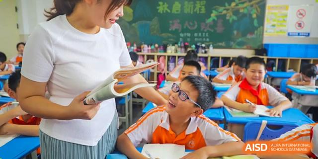 A teacher from Changsha Lushan Zhongjia School interacting with an excited, smiling male student wearing an orange and white shirt, who is looking up at the book the teacher is holding.