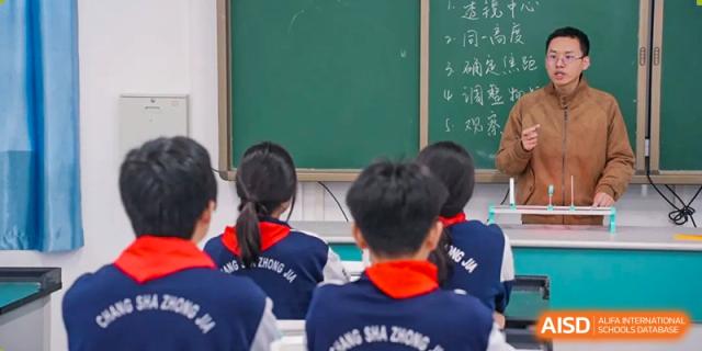 A view of students from Changsha Lushan Zhongjia School seated in a classroom, with the backs of their uniform jackets visible as they face the green chalkboard.
