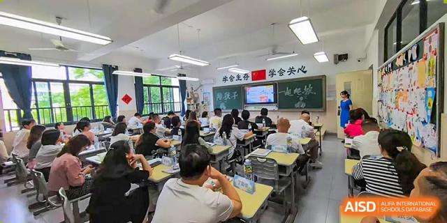Students and adults seated in a classroom at Changsha Lushan Zhongjia School, watching a presentation projected onto a large screen at the front of the room.