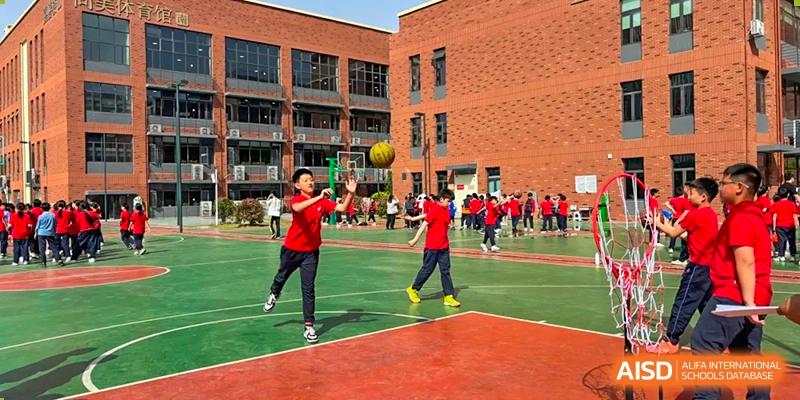A student from Changsha Lushan Zhongjia School throwing a ball on a multi-colored outdoor sports court with the modern brick school building in the background.