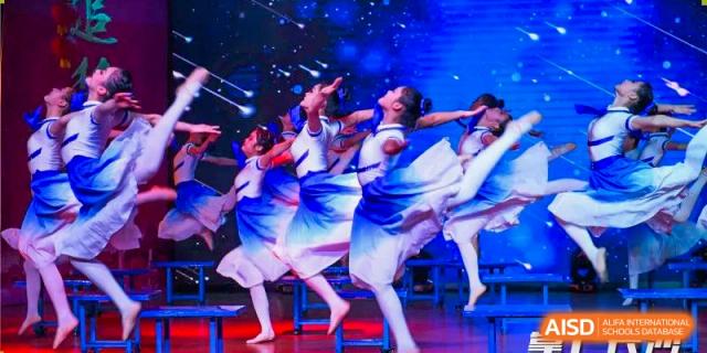 A dynamic shot of a group of students from Changsha Lushan Zhongjia School performing a synchronized dance routine on a stage with a bright blue background.
