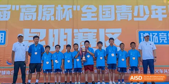 A group of male students from Changsha Lushan Zhongjia School in blue uniforms standing together, celebrating a sports victory with a trophy or award.