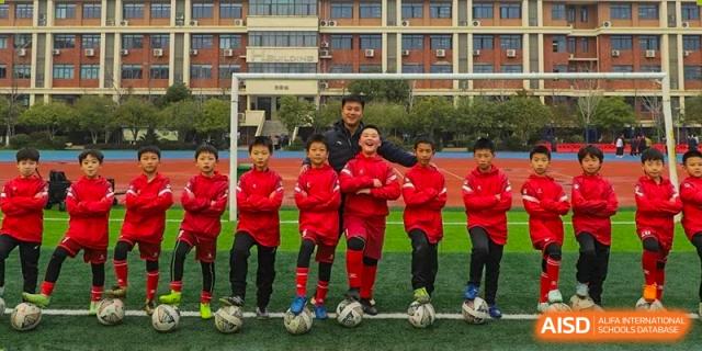 A soccer team from Changsha Lushan Zhongjia School in red uniforms posing for a group photo with a coach, with soccer balls resting at their feet.