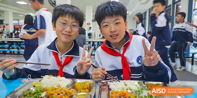 Two happy students from Changsha Lushan Zhongjia School wearing their red neck scarves, enjoying a meal together in the school cafeteria.