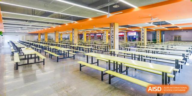 A wide shot of the large, empty dining hall or cafeteria at Changsha Lushan Zhongjia School, featuring rows of long yellow tables and benches.