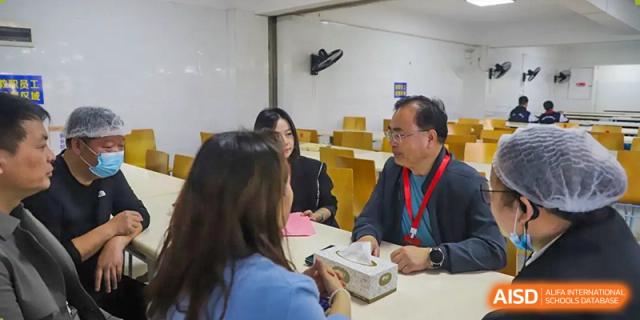 Adults, likely staff or guests of Changsha Lushan Zhongjia School, sitting at a table having a discussion over a meal in the dining area.