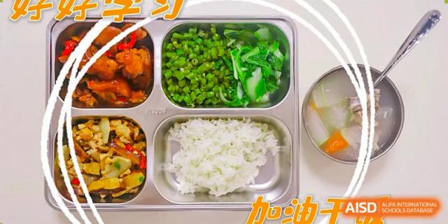 A metal segmented lunch tray from Changsha Lushan Zhongjia School containing white rice and a serving of green beans or chopped vegetables, with other dishes visible in different sections.
