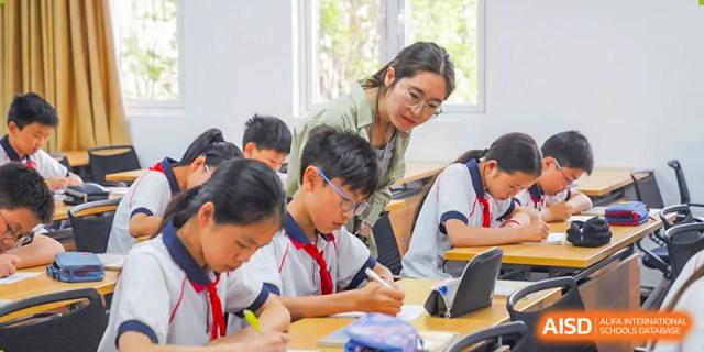 A female teacher helps a group of students with their work at a desk, at Changshu Lunhua Foreign Language School.