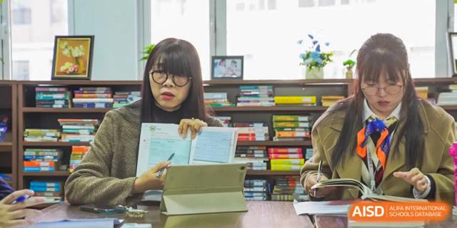 Two female students study together at a table, surrounded by books on shelves, at Changshu Lunhua Foreign Language School.