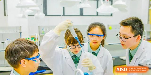 Two female students in lab coats conduct a science experiment with beakers and pipettes, at Changshu Lunhua Foreign Language School.