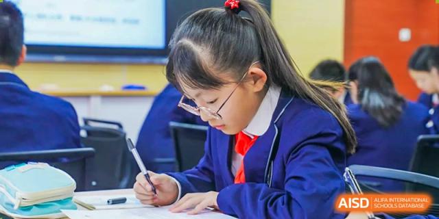 A young female student in glasses writes in a notebook at her desk, at Changshu Lunhua Foreign Language School.