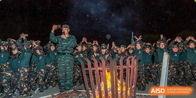 A group of students in military uniforms stand around a campfire at night, with Changshu Lunhua Foreign Language School.
