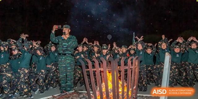 A group of students in military uniforms stand around a campfire at night, with Changshu Lunhua Foreign Language School.