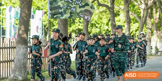 A group of students in military-style uniforms run outdoors, with Changshu Lunhua Foreign Language School.