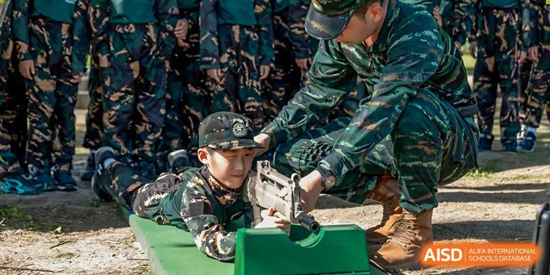 A young boy in military fatigues is being taught to handle a rifle by an instructor, at Changshu Lunhua Foreign Language School.