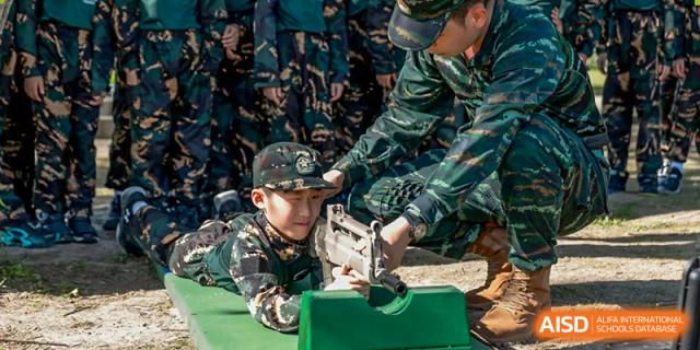 A young boy in military fatigues is being taught to handle a rifle by an instructor, at Changshu Lunhua Foreign Language School.