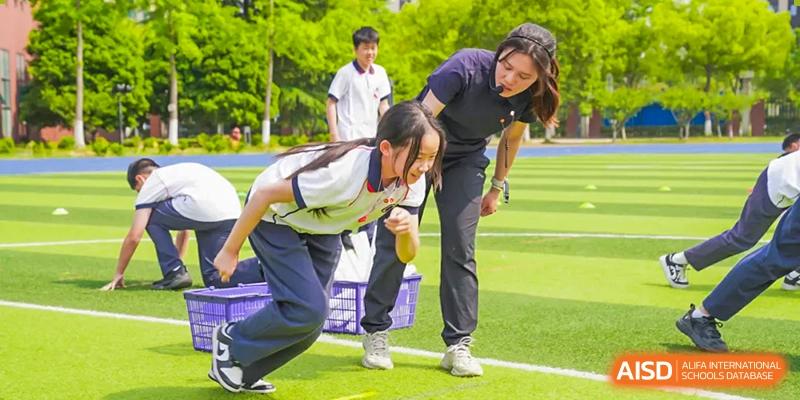 Two female students and one male student are on a sports field, with one female student helping another, at Changshu Lunhua Foreign Language School.