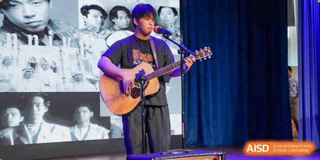 A male student plays an acoustic guitar and sings into a microphone on a stage, at Changshu Lunhua Foreign Language School.