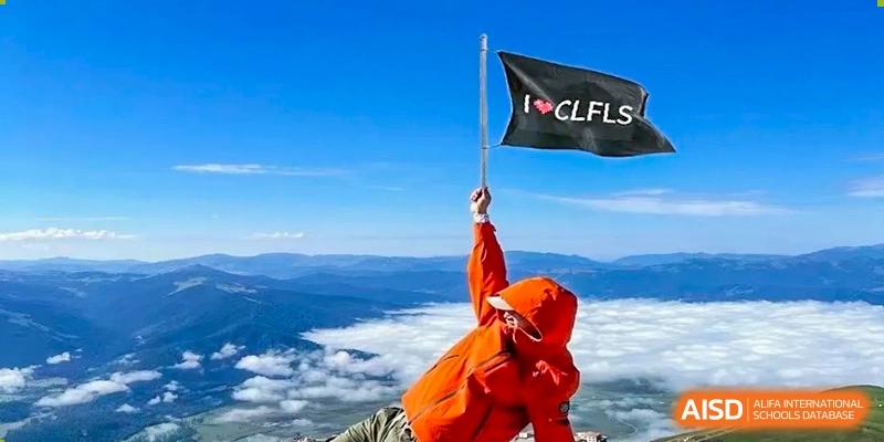 A person in a red jacket stands on a mountain peak holding a flag, at Changshu Lunhua Foreign Language School.