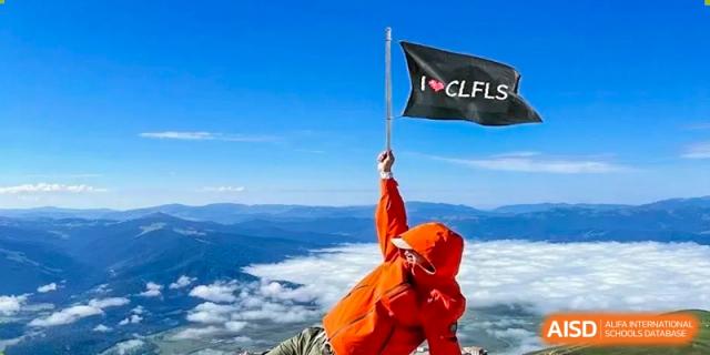 A person in a red jacket stands on a mountain peak holding a flag, at Changshu Lunhua Foreign Language School.
