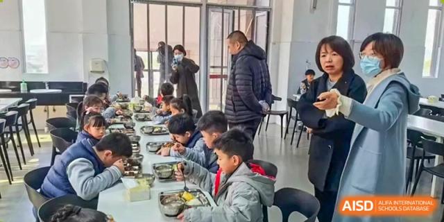 Students seated at a long table eating a meal in a cafeteria, at Changshu Lunhua Foreign Language School.