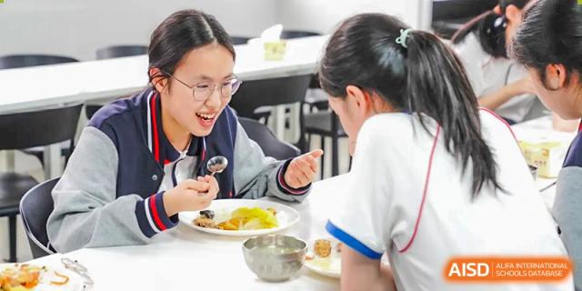 Two female students eat together at a table in the cafeteria, at Changshu Lunhua Foreign Language School.