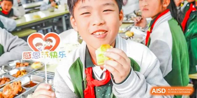 A young boy smiles for the camera while holding a piece of food, at Changshu Lunhua Foreign Language School.