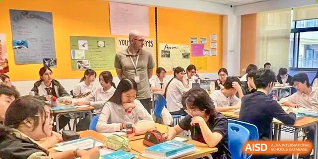 A teacher observing students as they work intently on books and paper assignments in a classroom at Chiway Bilingual School Xiamen.