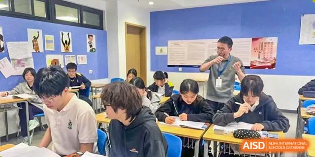 A teacher assisting students working on individual assignments in a modern classroom environment at Chiway Bilingual School Xiamen.