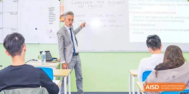 A male teacher at Chiway Bilingual School Xiamen pointing toward notes on a whiteboard while giving instruction to the class.