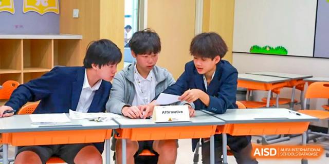 A small group of students from Chiway Bilingual School Xiamen collaborating and reviewing materials together at a desk.
