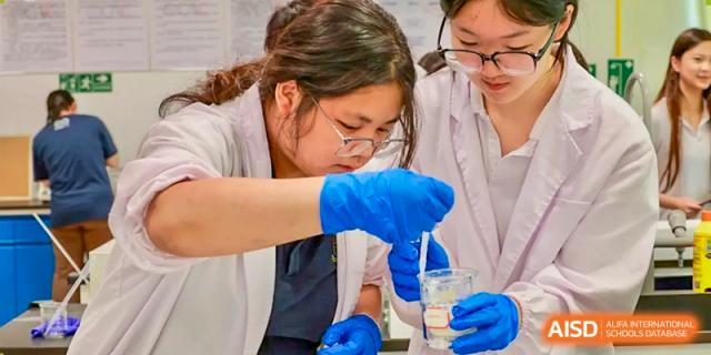 Students from Chiway Bilingual School Xiamen wearing lab coats and blue gloves, performing a chemical or science experiment.