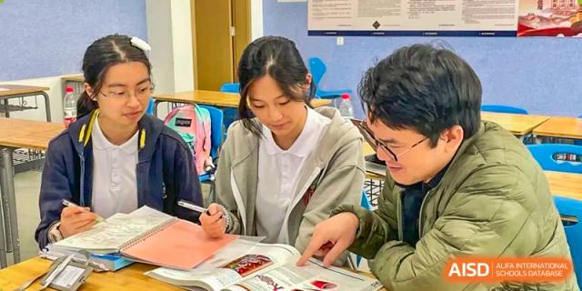 Two students from Chiway Bilingual School Xiamen collaborating closely while reviewing a textbook and notes together.