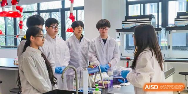 A small group of male students from Chiway Bilingual School Xiamen wearing lab coats and safety gloves, observing a science experiment setup.