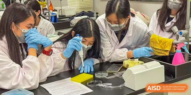 Two female students from Chiway Bilingual School Xiamen wearing protective gear while performing a biological experiment in a lab.